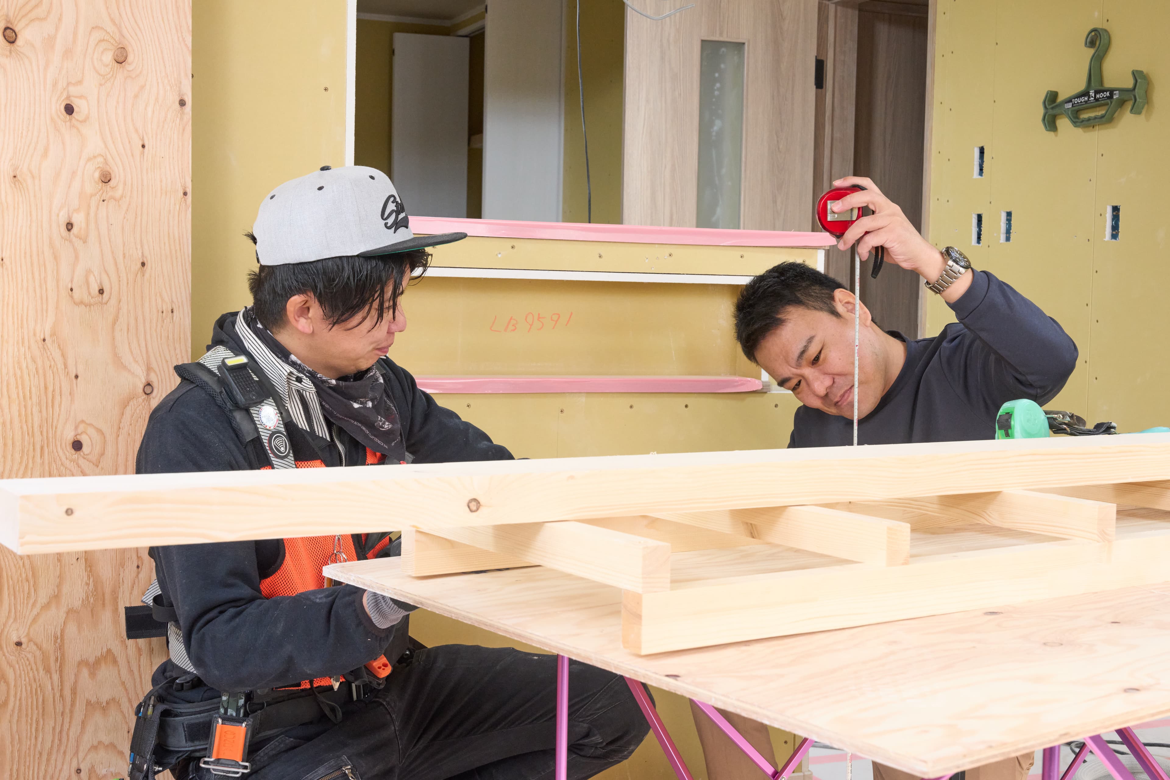 代表が現場で職人と向かい合い、アルミパーツの試作品を手に持ちながら真剣に議論している様子